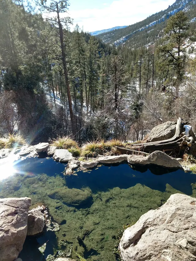 Clear natural hot spring pool at Spence Hot Spring with rocky edges and tall pine trees in the background near Jemez Springs New Mexico.