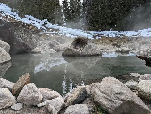 Snow-covered natural hot spring pool steaming quietly, surrounded by rocks and forest at Jerry Johnson Hot Springs, Kooskia, Idaho.