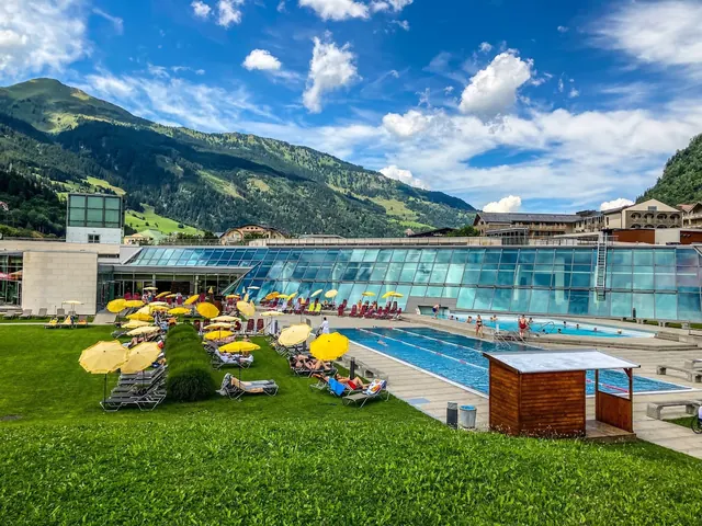 Outdoor spa pool at Alpentherme Gastein with bright yellow umbrellas and loungers under a blue sky near Bad Hofgastein, Austria.