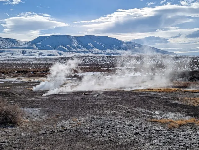 Steam rising from vents across the rocky ground of Mickey Hot Springs with snowy mountains in the background near Burns Oregon.