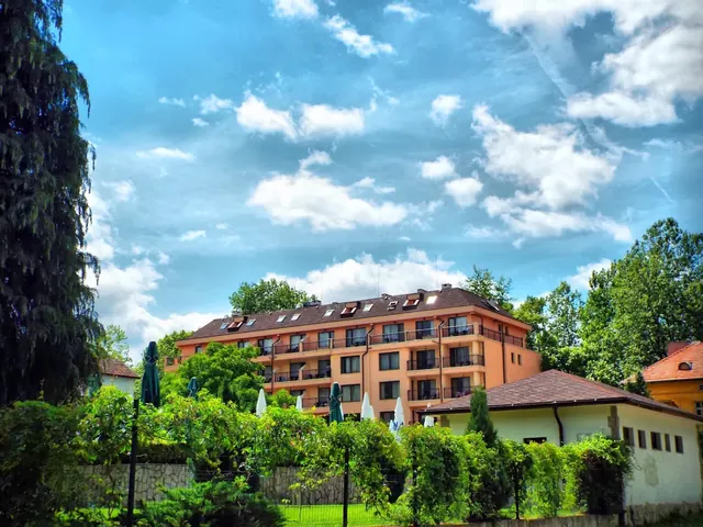 Four-story beige hotel building with green trees and blue sky in Varshets near SPA Hotel Medicus hot springs in Bulgaria.