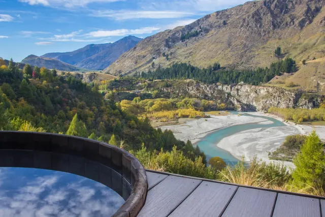 Wooden soaking pool at Onsen Hot Pools with clear water reflecting mountains and river valley near Queenstown New Zealand.