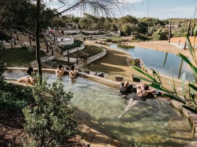 Multi-tiered hot spring pools with people soaking and wooden railings around the area at Peninsula Hot Springs in Fingal, Mornington Penins.