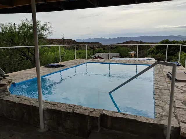 Covered hot spring pool with stone edge and handrail at Chinati Hot Springs, showing distant mountains and cloudy sky near Presidio, Texas.