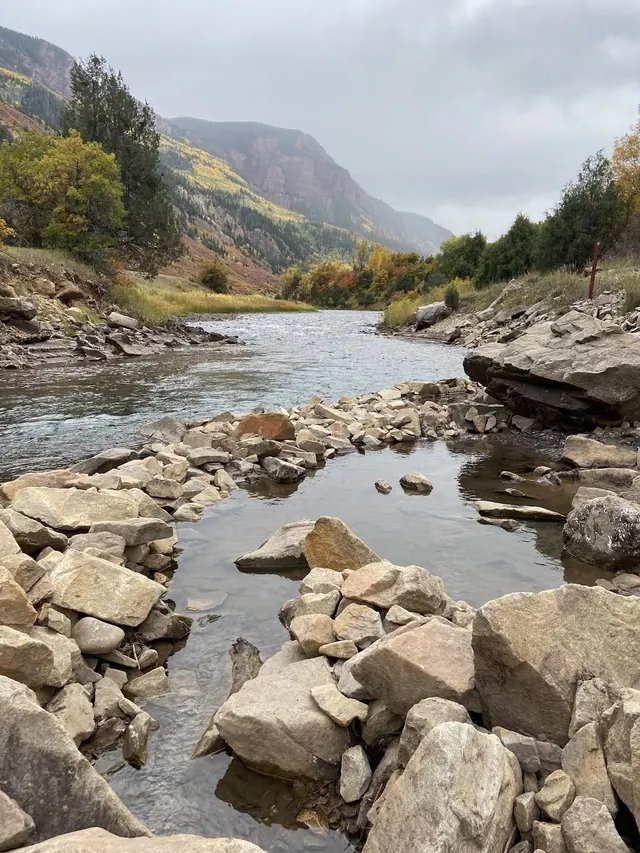 Rocky natural hot spring pools alongside a flowing river with forested hills in the background at Penny Hot Springs, Colorado.