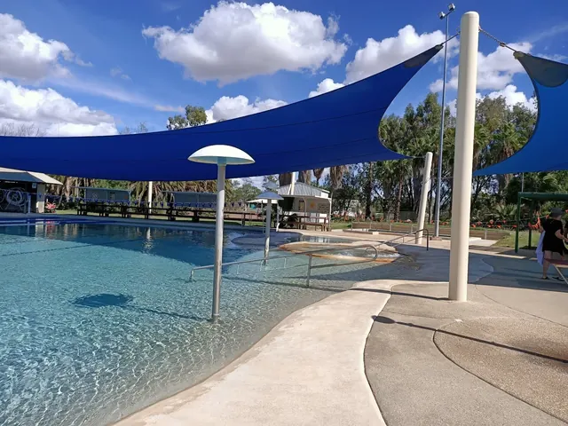 Shallow outdoor mineral pool with calm waters shaded by blue canopies and surrounded by greenery at Blackall Aquatic Centre.