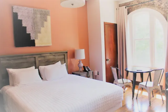 Bedroom with king-size bed, white bedding, a wooden headboard, orange accent wall, and a table with two metal chairs.