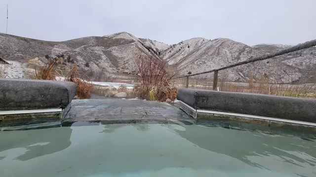 Clear water of an outdoor spa pool at Astoria Hot Springs with snow-dusted hills and dry vegetation near Jackson, Wyoming.