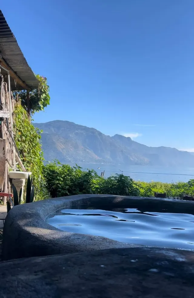 Calm water of an outdoor hot spring pool at Los Termales reflecting blue sky and mountain views near San Pedro La Laguna, Guatemala.