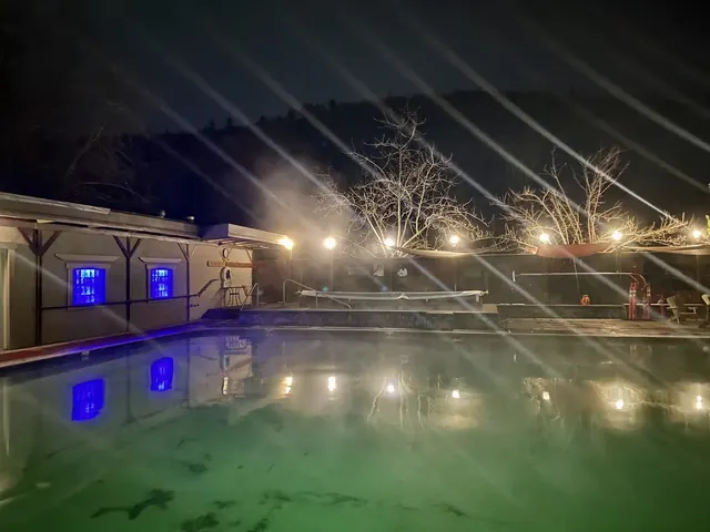 Night view of steamy hot spring pool at Jackson Wellsprings illuminated by string lights with bare trees in the background.