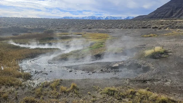 Steaming mineral pools and wet ground surrounded by sparse vegetation at Mickey Hot Springs with distant mountains near Burns Oregon.
