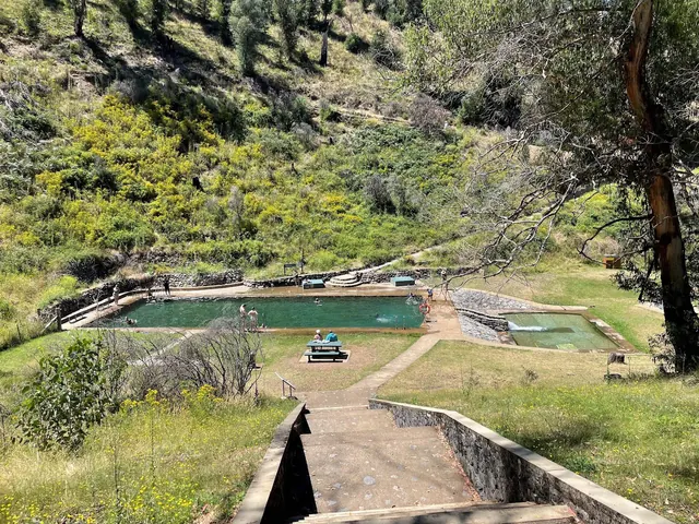 Yarrangobilly Caves thermal pool features an outdoor soaking pool with steps and picnic tables surrounded by green grassy areas and trees n.