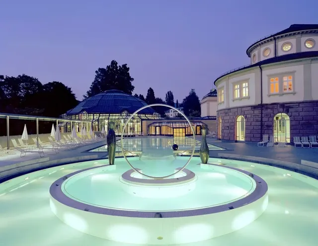 Night view of a circular pool with art installation and illuminated water at Cassiopeia Therme Badenweiler in Badenweiler, Germany.