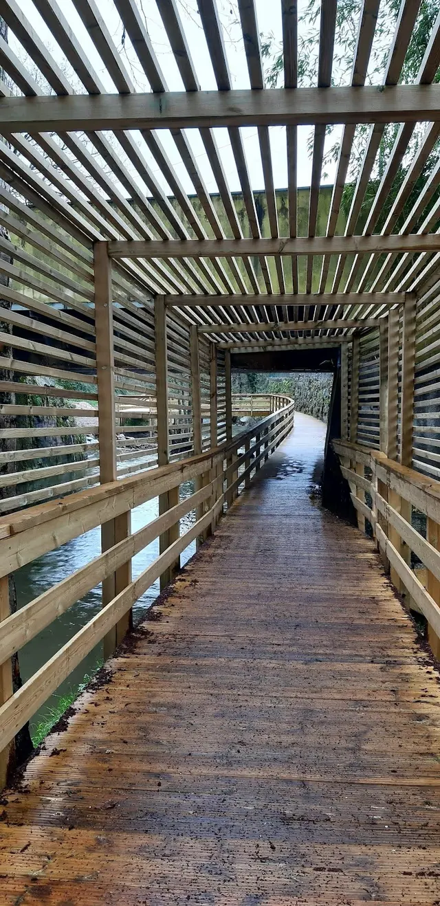 Wooden covered boardwalk over water with vertical and horizontal slats creating a patterned shadow walkway in Vizela, Portugal.