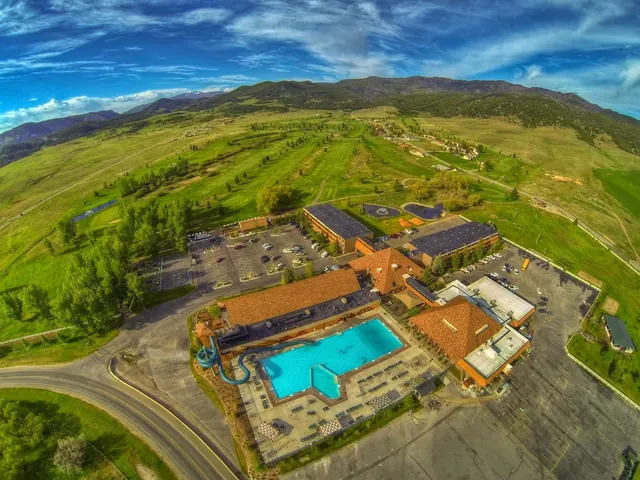Aerial view of Fairmont Hot Springs Resort in Anaconda showing an outdoor pool, water slide, parking lot, and green mountains.