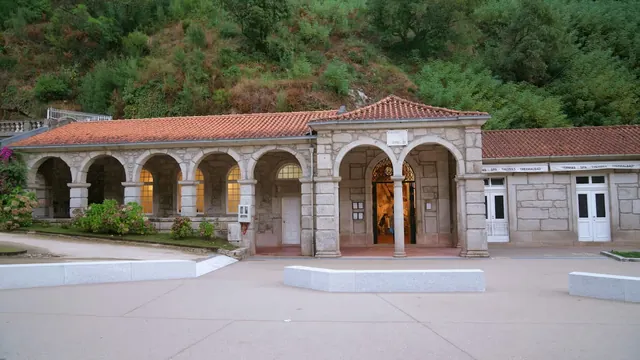 Stone spa building with multiple arches and a tiled roof surrounded by greenery at Termas do Geres in Geres Portugal.