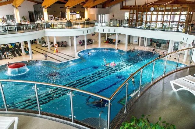 Indoor swimming pool with a large open area, surrounded by a balcony and wooden ceiling beams at Termy BUKOVINA in Bukowina Tatrzanska Pola.