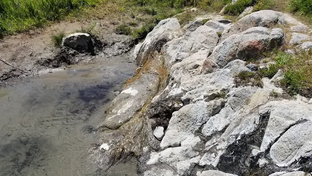 Rock-lined natural hot spring pool filled with clear water at Cove Creek Hot Springs near Stanley, Idaho, surrounded by green vegetation