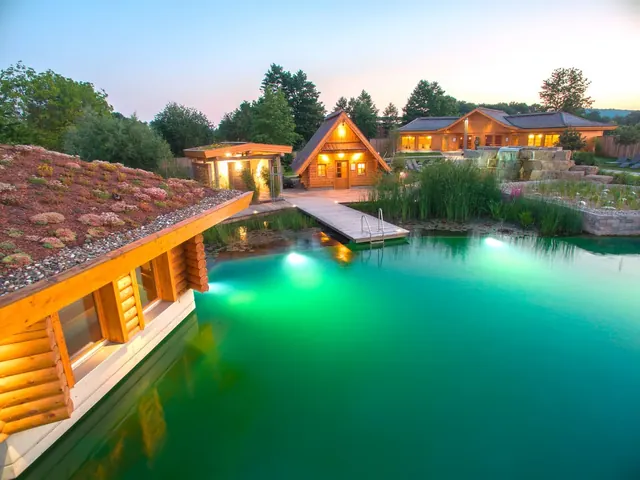 Natural outdoor pool with turquoise water surrounded by wooden cottages and green plants at Obermain Therme in Bad Staffelstein Germany.