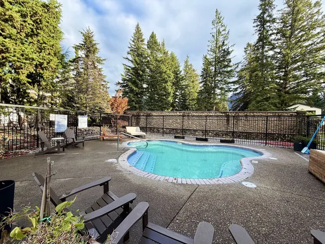 Clear blue outdoor mineral pool with Adirondack chairs and tall evergreen trees behind a metal fence at Bonneville Hot Springs in Washingto.