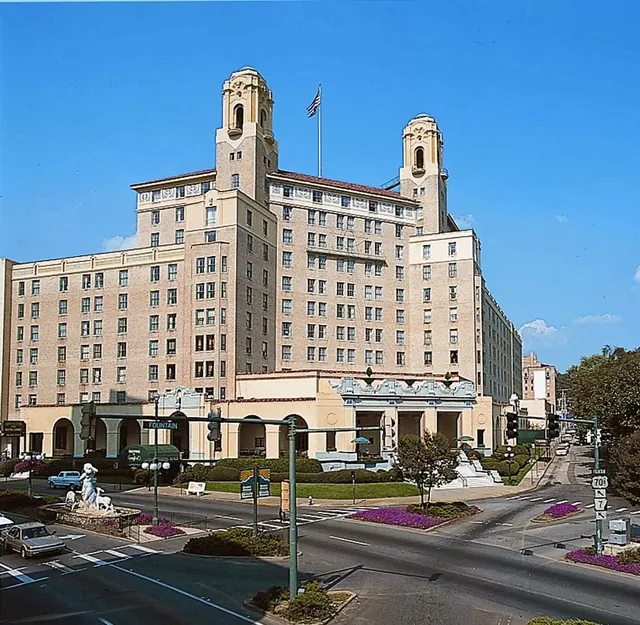 Historic beige brick building of Arlington Resort Hotel & Spa in Hot Springs Arkansas seen from across a busy street with traffic lights.