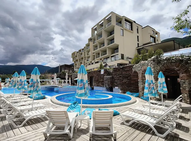 Blue-tiled circular mineral pool surrounded by lounge chairs and umbrellas at Aqua Club Kotvata with resort building in Sapareva Banya.