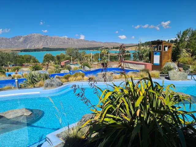 Curved pools at Tekapo Springs offer views of Lake Tekapo and distant mountains with surrounding plants and rock features in New Zealand.