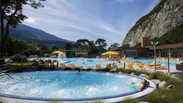People relaxing in the large outdoor pool with yellow umbrellas and lounge chairs at Les Bains de Lavey near Saint-Maurice Switzerland.