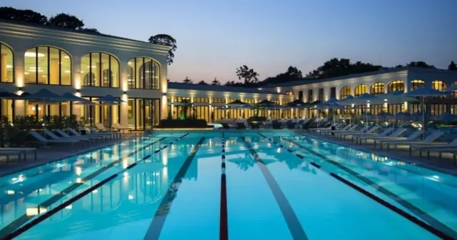 Night shot of outdoor swimming lanes pool at Aquahouse Thermal and Beach with glowing blue water and illuminated large building in Saints C.