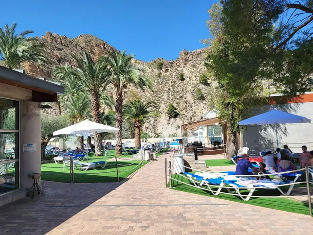 Outdoor pool area with blue lounge chairs and white umbrellas at Balneario de Archena surrounded by rocky hills in Murcia Spain.