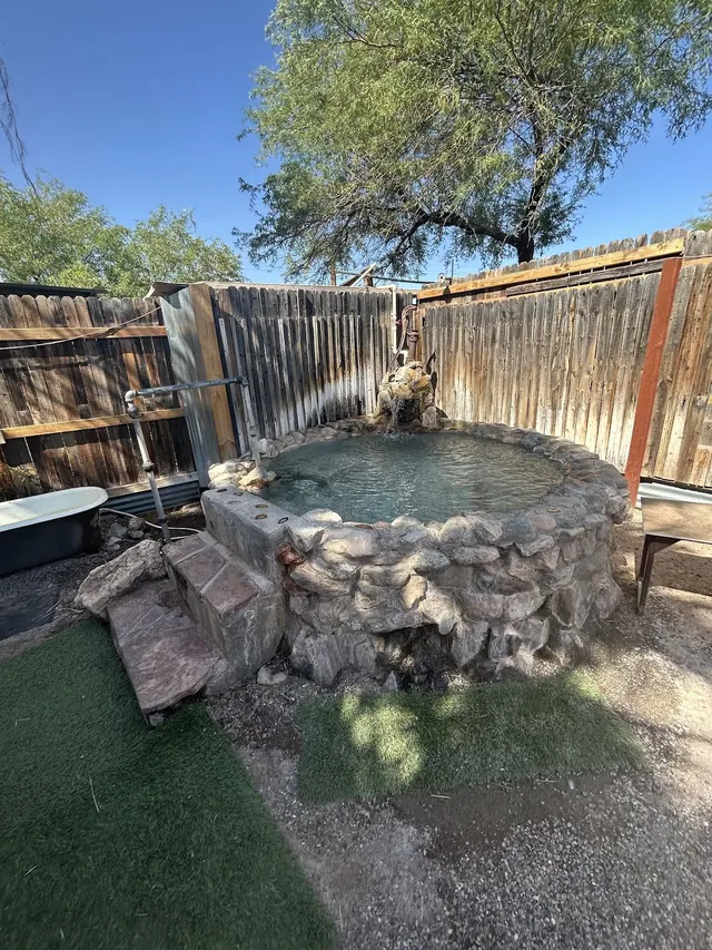 Small round stone soaking pool with handrails and wooden fence enclosure at El Dorado Hot Springs in Arizona.