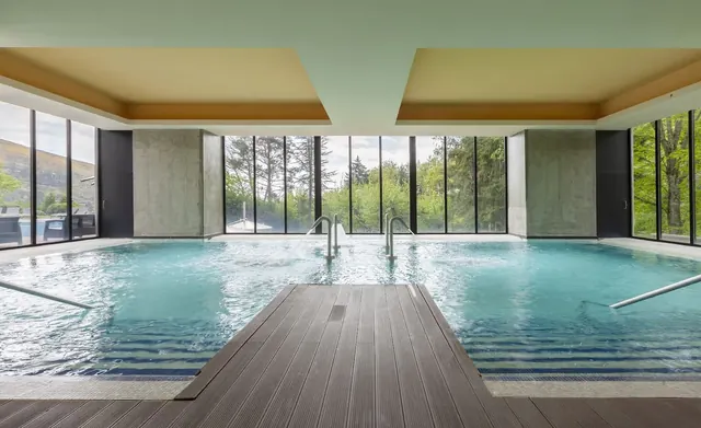 Wide indoor mineral pool at Aquadome in Unhais da Serra portugal featuring clear water, wooden deck, and large windows overlooking green hi.