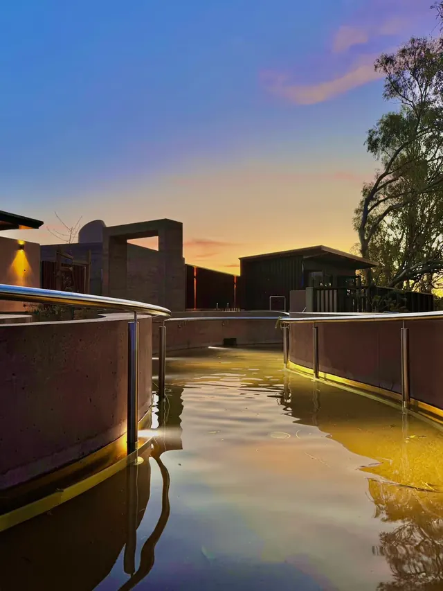 Evening light illuminating shallow mineral pools with handrails and modern buildings at Cunnamulla Hot Springs located in Cunnamulla Queens.