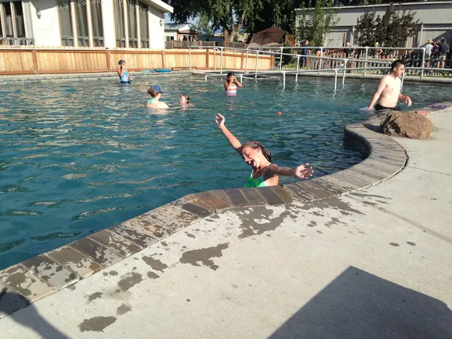 Visitors including children having fun in the large outdoor Mundo Hot Springs pool located next to wooden buildings in Cambridge, Idaho.