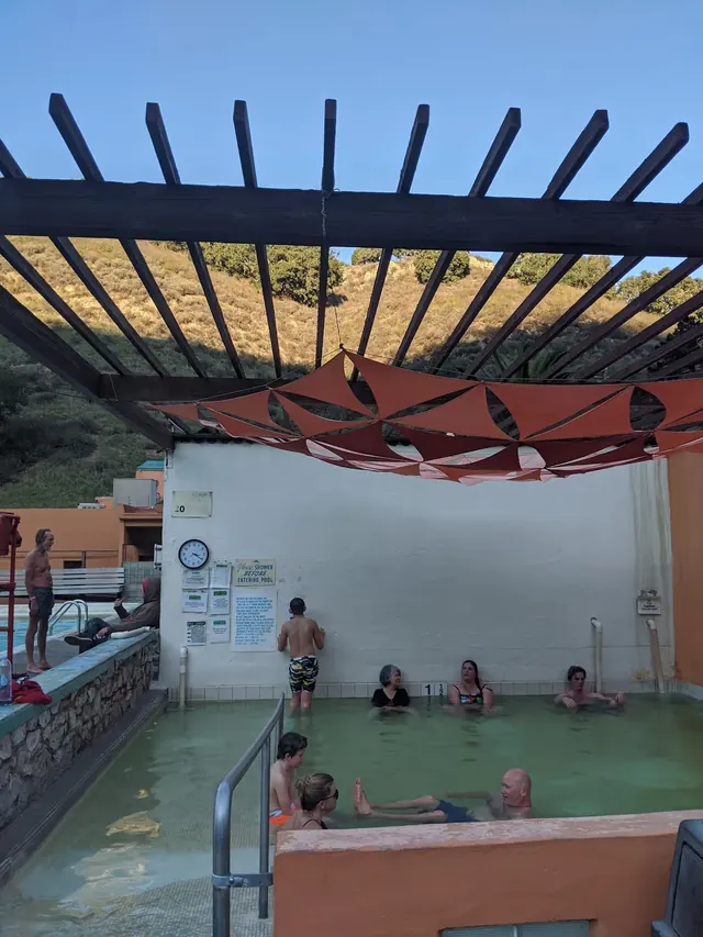 Indoor mineral hot spring pool at Avila Hot Springs with people soaking and a shaded beam structure overhead in California.