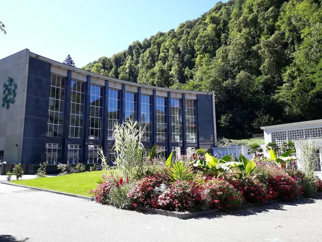 Modern curved building with tall glass windows and green forested hill behind at Thermes de Luchon near Bagneres-de-Luchon, France.