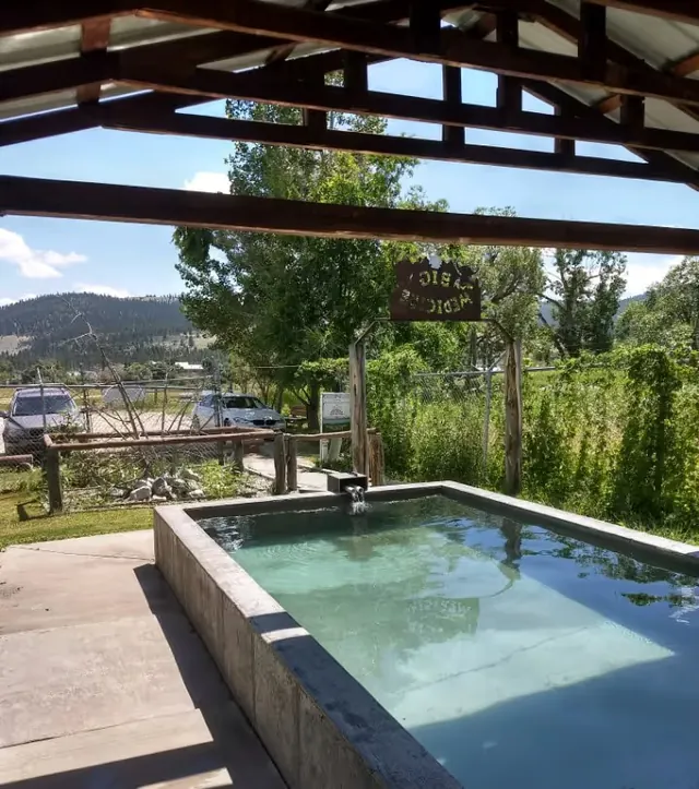 Small rectangular soaking pool with clear water under a shaded structure at Big Medicine Hot Springs, Montana.