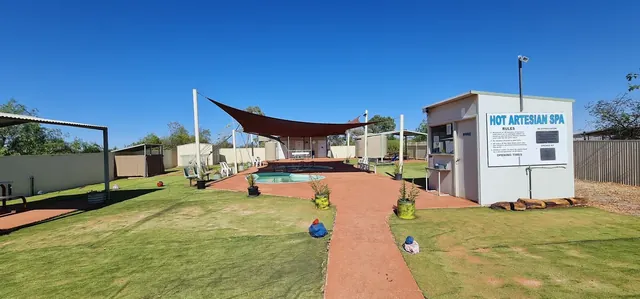 Wide view of Yowah Artesian Pools area showing multiple soaking pools surrounded by lawn and a shaded canopy on a sunny day.