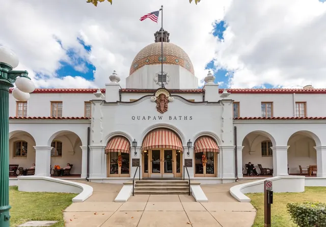 White building with a terracotta dome and arched windows housing Quapaw Baths, located in Hot Springs, Arkansas under a cloudy sky.