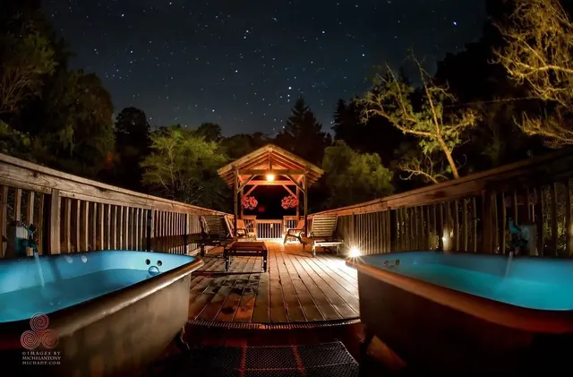 Two outdoor spa tubs filled with water glow softly under starry night sky on a wooden deck at Orr Hot Springs.