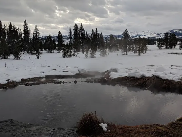 Steaming natural hot spring pool at Polecat Hot Springs with snowy ground and distant mountains near Moran, Wyoming.
