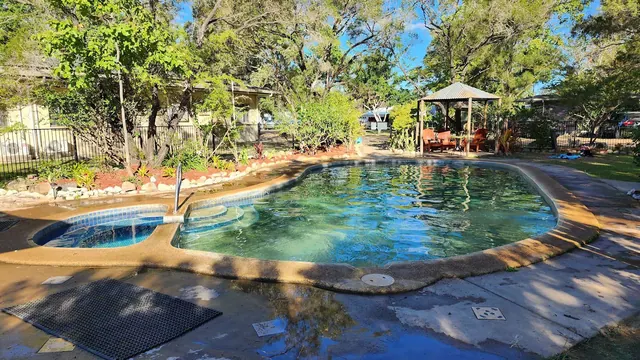 Clear water fills a natural hot spring pool with stone edging and green trees in the background at Innot Hot Springs Caravan Park.