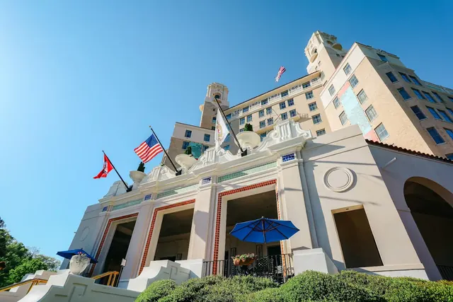 Low angle view of Arlington Resort Hotel & Spa facade in Hot Springs Arkansas featuring flags, balconies, and a blue umbrella on terrace.