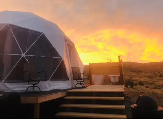White soaking tubs on a raised wooden platform beside a dome tent under a colorful sunset at Pipestone Hot Springs near Whitehall Montana.