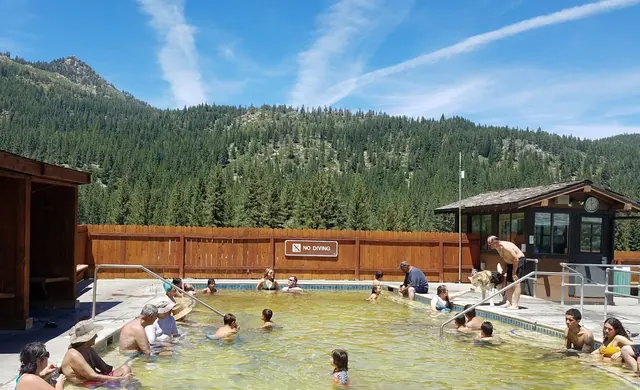 Bathers relaxing in the shallow Grover Hot Springs State Park mineral pool with a wooden fence and pine forest in Markleeville California.