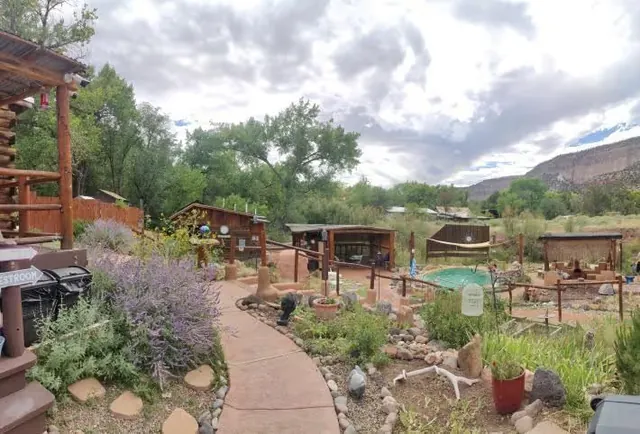 Panoramic view of Jemez Hot Springs soaking area with a garden pathway, several small wooden shelters, and lush trees in Jemez Springs New.