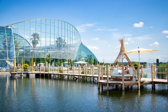 Outdoor spa pool at Thermen & Badewelt Sinsheim featuring a wooden boardwalk, sunshade umbrellas, and a reflective water pond in Sinsheim G.