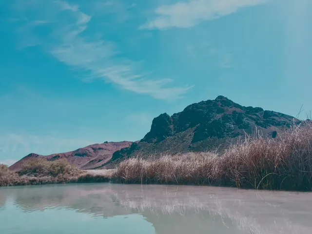 Natural steaming pool at Black Rock Hot Springs with dry grass and rugged mountain under clear blue sky near Gerlach, Nevada