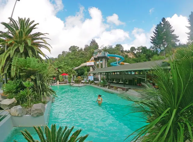 Large turquoise hot spring pool with water slide tower and lush greenery around at Taupo DeBretts Hot Springs near Taupō New Zealand.
