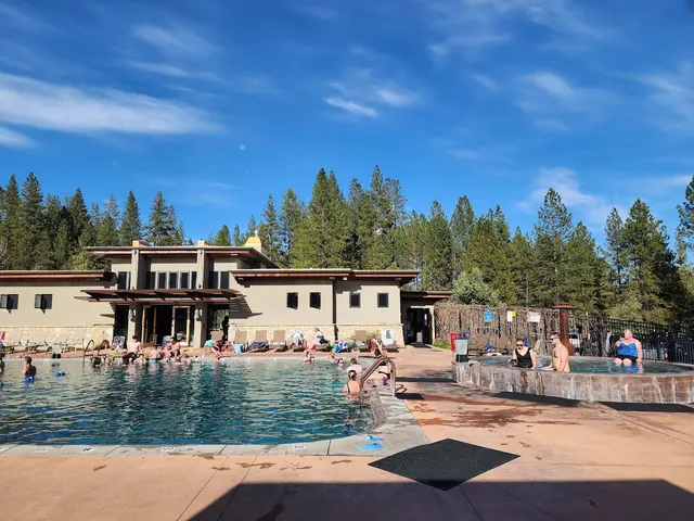 Daytime scene of people enjoying outdoor pools surrounded by forest near the main building at The Springs, Idaho City, Idaho.